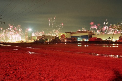 Das Bild zeigt Feuerwerk über einem Industriegelände. Der Boden ist rot eingefärbt.