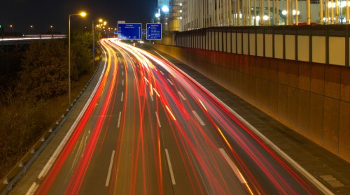 Die Nachtaufnahme zeigt die Fahrspur einer Autobahn mit Abfahrt, man kann die Rücklichter der Autos als Spuren sehen