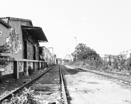 Das s/w-Foto zeigt eine verlassene Bahnstrecke, auf der rechten Seite ist ein mit Graffiti beschmierter Güterschuppen.