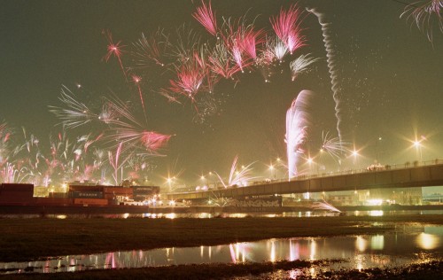 Das Bild zeigt Feuerwerk über einer Brücke und Hafengelände, wo Container stehen.