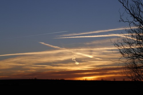 Das Foto zeigt den Sonnenuntergang, die Sonne ist fast ganz weg, man sieht Kondensstreifen