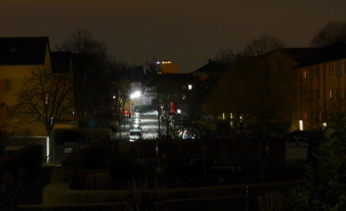 Das Bild zeigt die Nachtaufnahme einer Wohnstraße, rechts und links der Straße stehen gebe Mehrfamilienhäuser