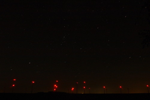 Man sieht dan Himmel, die Sterne bilden kurze Linien. Von den Windkraftanlagen sieht man die roten Positionslichter sehr deutlich.