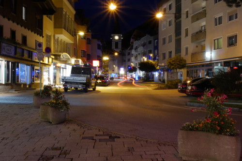 Das Bild zeigt die Bahnhofsstraße, eine Einkaufsstraße in Wörgl, bei Nacht. Die Lichter der Autos haben Spuren hinterlassen.. Im Hintergrund sieht man die Stadtkirche von Wörgl