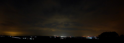 Das Bild zeigt eine Nachtaufnahme-Panoramaufnahme, man sieht die Stadt Schöningen, ein paar andere Dörfer, in der Mitte den Schornstein vom Kraftwerk Buschhaus und auf der rechten Seite Positionslichter von Windkraftanlagen.