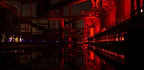 Das Bild ist in der alten Kokerei Zollverein aufgenommen, es zeigt die Industrieanlagen bei Nacht, die rot beleuchtet sind.