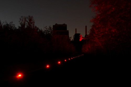 Das Bild zeigt die rot beleuchteten Gebäude und die roten Markierungsleuchten eines Fußweges in der Zeche Zollverein