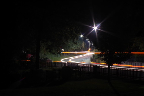 Das Foto zeigt die Hauptstraße in Winnigstedt, das Bild ist durch die Bäume aufgenommen. Man sieht die Streifen von Fahrzeuglichtern.