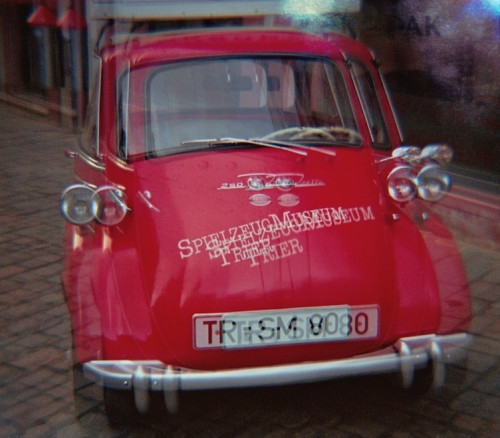 Das Bild ist eine verwackelte/mehrfachbelichtete Aufnahme von einem roten GoGo, einem Werbefahrzeug vom Spielzeugmuseum Trier