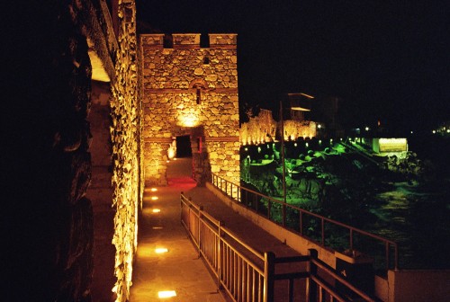 Das Foto zeigt die gelb und grün ausgeleuchtete Stadtmauer von Sozopol und den Fußgängerweg an der Mauer