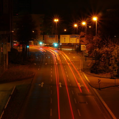 Das Foto zeigt eine Nachtaufnahme von einer Straße in Essen, die Autos fahren alle von dem Fotografen weg, daher sieht man nur die Rücklichter als rote Streifen (und teilweise die Blinker als gelbe Streifen). E ist eine Mehrspurige Straße, bei der man in verschiedene Richtungen abbiegen kann.