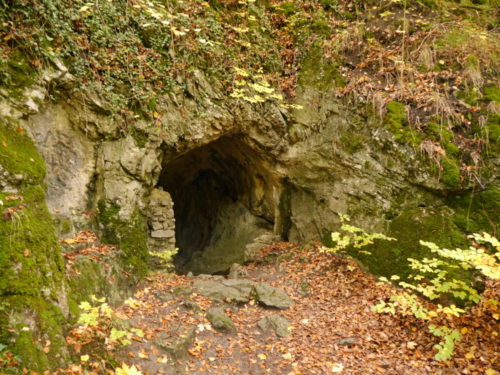 Der Eingang vom Volkmarskeller, einer Kaarsthöhle. Man sieht drim herum Fels, Moos und Blätter, die herbstlich verfärbt sind.