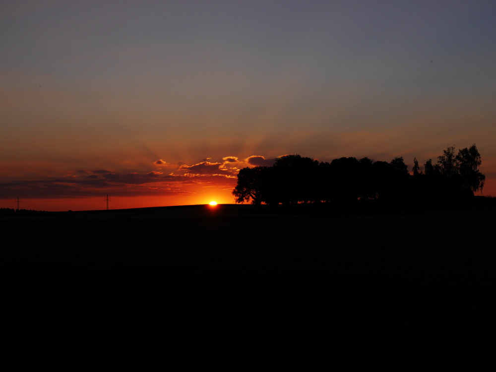 Das Foto zeigt, wie die Sonne links neben dem Winnigstedter Friedhof untergeht