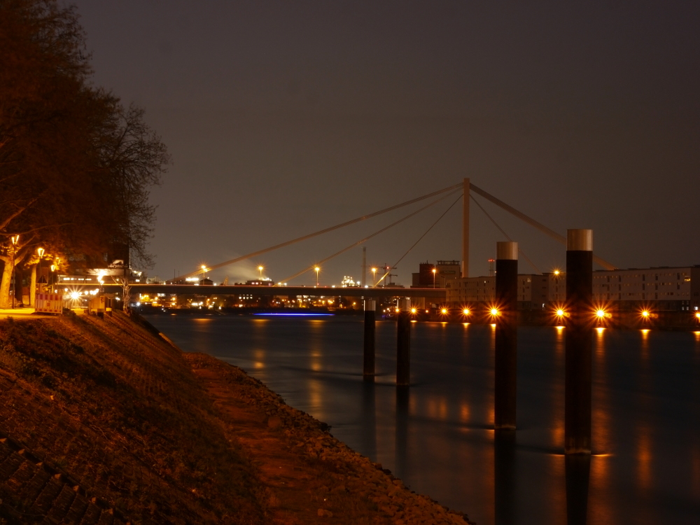 Nachtfoto der Rheinbrücke zwischen Ludwigshafen und Mannheim, auf der rechten Seite sieht man die Striche von den Lichtern von Schiffen auf dem Rhein.