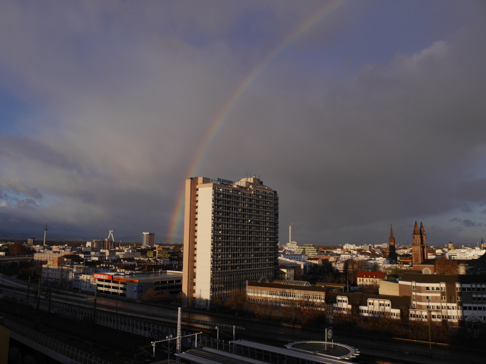 Das Foto zeigt einen Regenbogen über der Stadt Ludwigshafen, der Regenbogen kratzt die Spitze von einem Hochhaus.