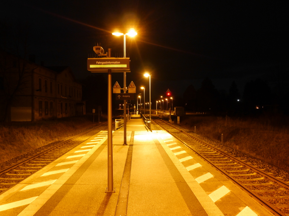 Der hell erleuchtete Mittenbahnsteig eines kleinen, menschenleeren Bahnhofs