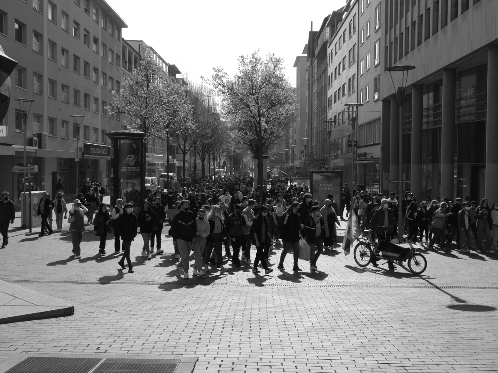 Das s/w-Foto zeigt den Demonstrationszug in der Innenstadt von Ludwigshafen von vorne, der Demo-Zug biegt gerade nach Links ab