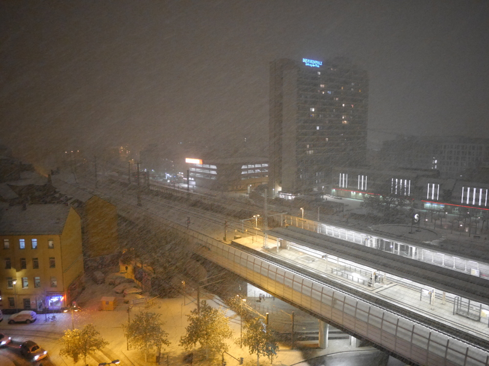 Das Foto zeigt die Stadt Ludwigshafen bei starkem Schneefall, man sieht den Bahnhof Mitte und die Bahntrasse, dahinter das Hochhaus it der "Rheinpfalz"-Werbung und viele Schneeflocken. Das Bild verschwindet auch in den Schneeflocken.