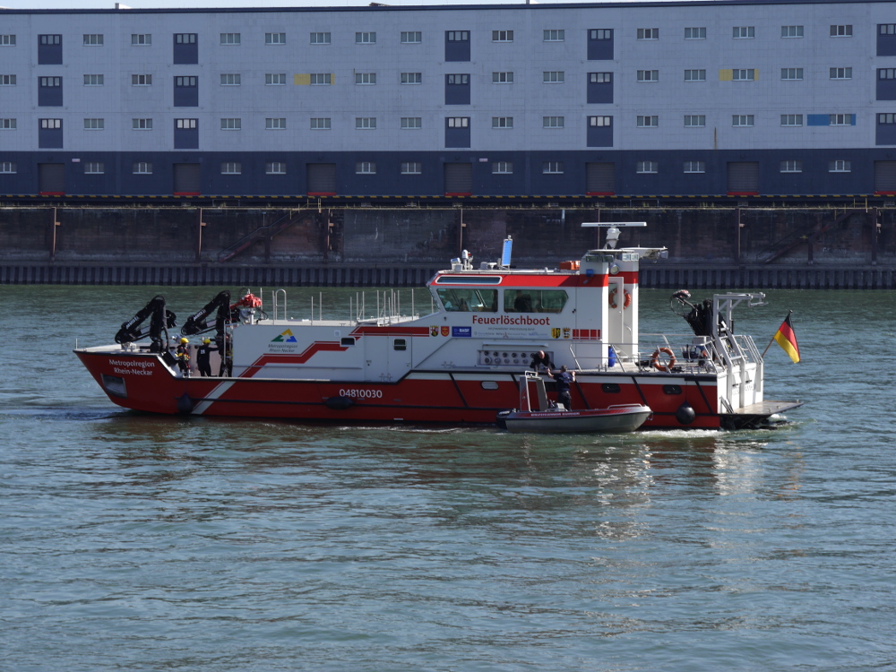 Ein großes Feuerlöschboot auf dem Rhein, an der Längsseite hat ein kleines Motorboot der Feuerwehr angelegt. Man erkennt Feuerwehrleute auf dem Boot.