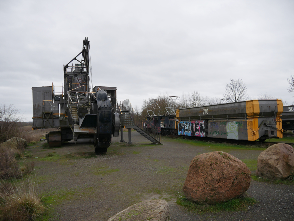 Das ausgestellte Gerät am Tagebau-Aussichtspunkt: links der alte Bagger, daneben die Lokomotive mit Wagen. Leider mit Graffiti beschmiert.