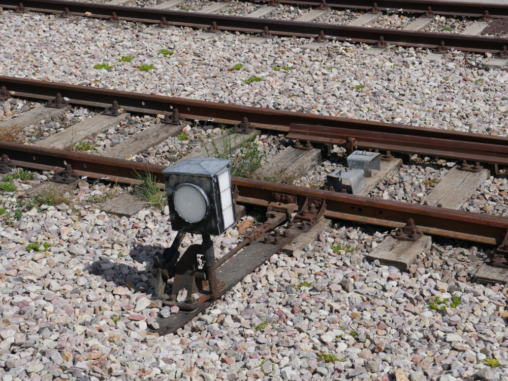 Das Foto zeigt eine alte, rostige Eisenbahn-Weiche mit Handantrieb und einer Weichenlaterne