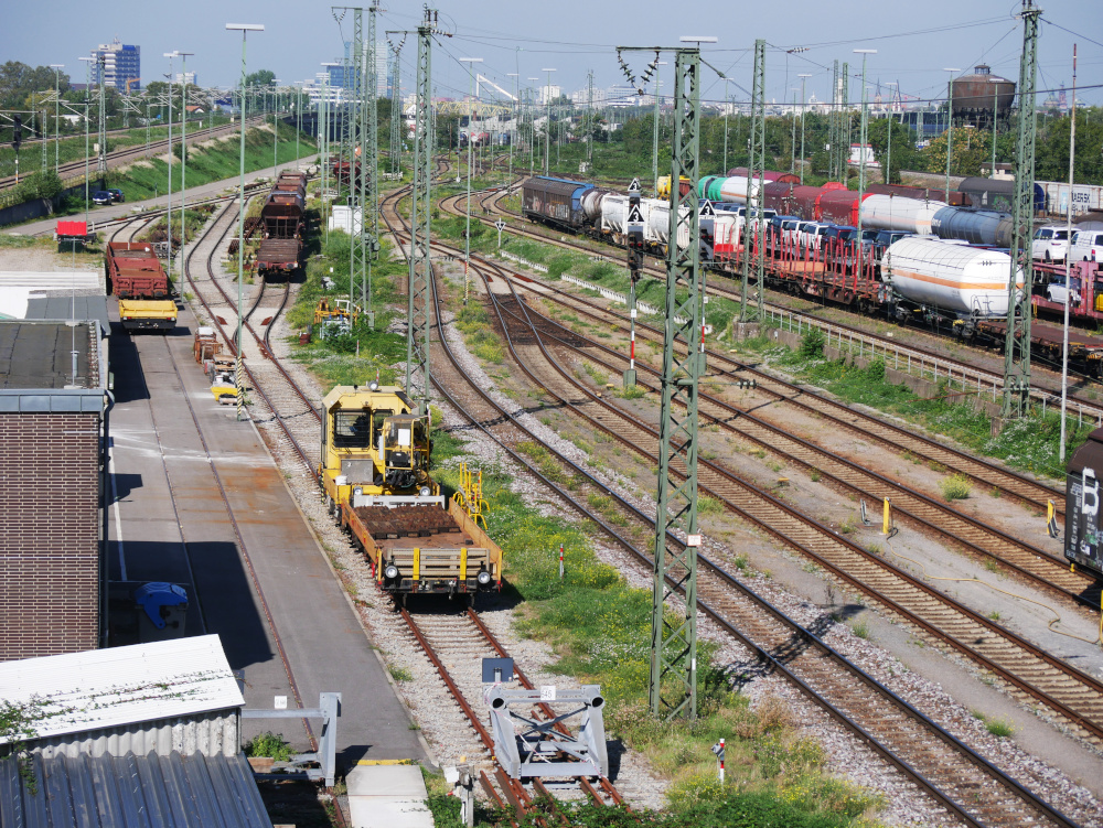 Das Foto zeigt eine Abstellanlage, man sieht auf der linken Seite abggestellte Bahn-Baufahrzeuge, auf der rechten Seite abgestellte Güterwaggongs.