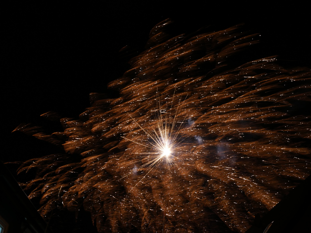 Das Foto zeigt die Explosion von Feuerwerksraketen am Himmel. Es sind viele Kleine Leuchtpunkte und Fäden dabei, was dem ganzen ein wenig den Eindruck eines astronomischen Bildes einer fernen Galaxi gibt.
