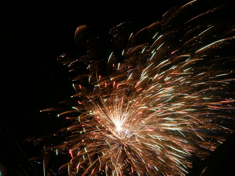 Ds Foto zeigt mehrere, bunte Feuerwerksexplosionen am Himmel, man sieht viele bunte Lichtspuren