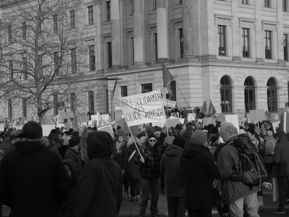 Das s/w-Foto wurde bei einer Demo gegen Rechtsextremismus am 20.01.2024 in Braunschweig aufgenommen. Ziemlich zum Rand der Demo steht ein Mann mit einem Transparent "Lieber solidarisch als solide Arisch"