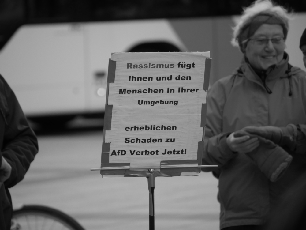 Das s/w-Foto wurde bei einer Demo gegen Rechtsextremismus und Fremdenhass am 03.02.2024 in Ludwigshafen aufgenommen. Es zeigt ein Papierschild an einem Stab: "Rassismus fügt Ihnen und den Menschen in Ihrer Umgebung erheblichen Schaden zu. AfD Verbot jetzt".