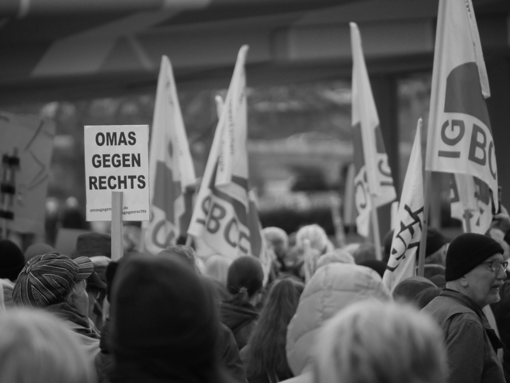 Das s/w-Foto wurde bei einer Demo gegen Rechtsextremismus und Fremdenhass am 03.02.2024 in Ludwigshafen aufgenommen. Im linken Bereich ist ein Pappschild "Omas gegen Rechts", rechts daneben Fahnen der Gewerkschaft IG BCE.