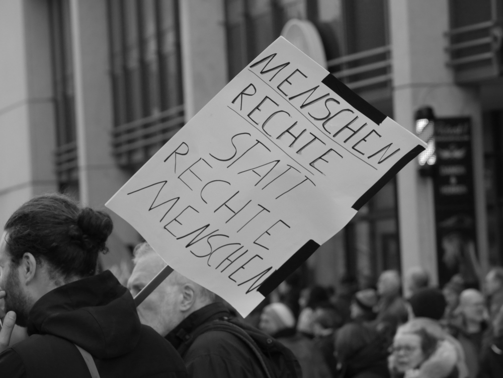 Das s/w-Foto wurde bei einer Demo gegen Rechtsextremismus und Fremdenhass am 03.02.2024 in Ludwigshafen aufgenommen. Es zeigt einen Demonstranten, der ein Schild mit dem Slogan "Menschenrechte statt rechter Menschen" über der Schulter trägt.