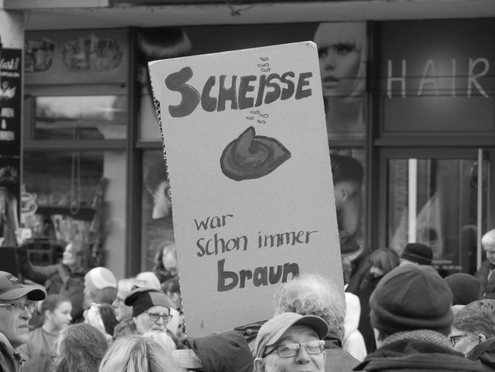 Das s/w-Foto wurde bei einer Demo gegen Rechtsextremismus und Fremdenhass am 03.02.2024 in Ludwigshafen aufgenommen. Man sieht ein Pappschild: "Scheisse (Kackhaufen) war schon immer braun"