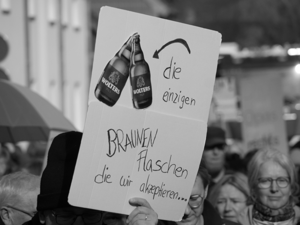 Das s/w-Foto stammt von einer Demo für Demokratie und gegen Rechtsextremismus. Es zeigt ein Plakat mit zwei Bierflaschen der regionalen Marke "Wolters" und dazu der Spruch "die einzigen Braunen Flschen diw wir akzeptieren".