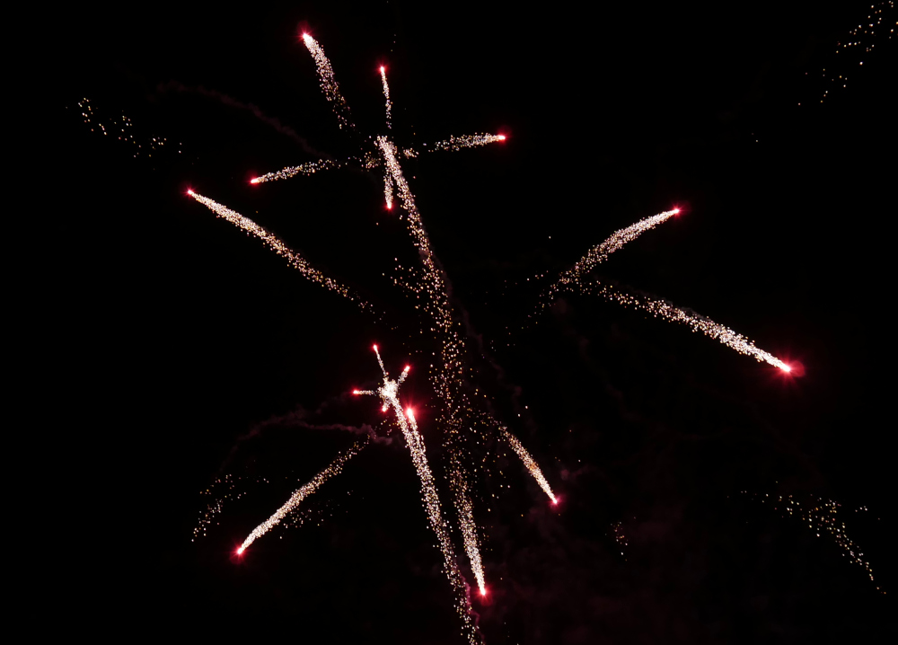 Das Foto zeigt Feuerwerk am Nachthimmel, weiße Streifen und rote Raketenköpfe.