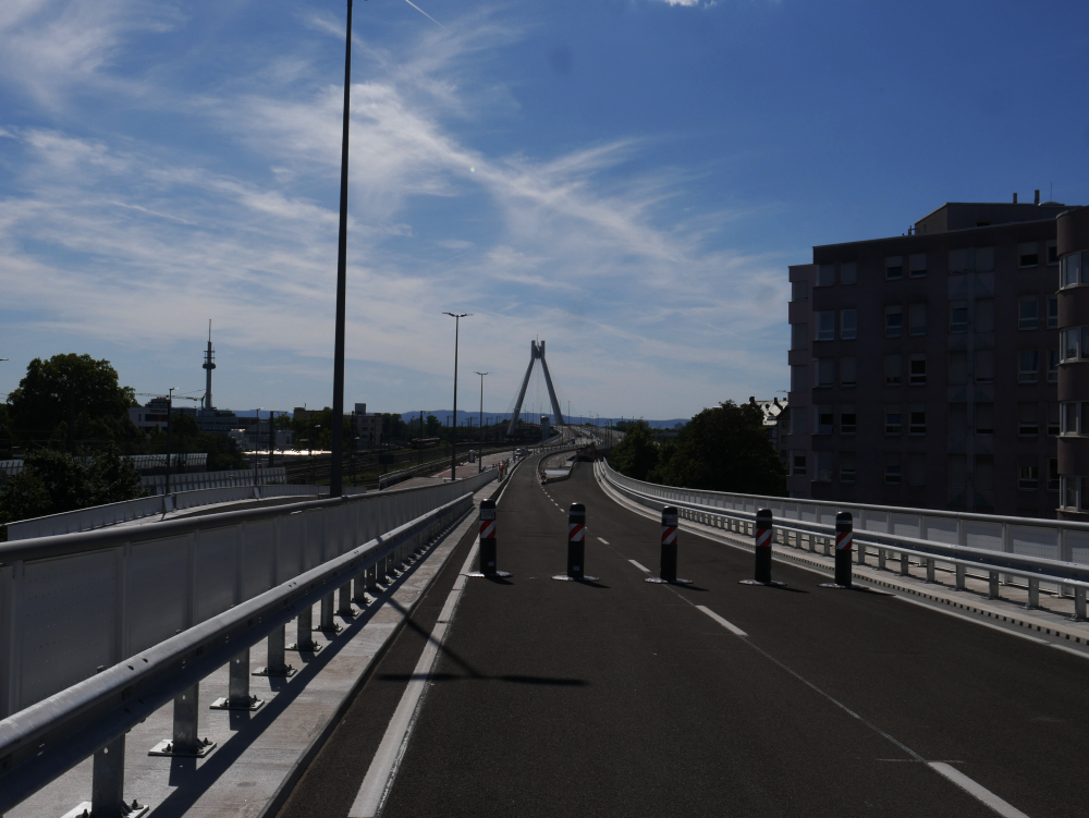 Das Foto zeigt am Ende des für Fußgänger*innen freigegebenen Bereichs den Blick in Richtung ludwigshafen Hauptbahnhof mit der markanten Brücke. Darüber der Blaue Himmel mit wenigen weißen Wolken. Auf der Straße stehen noch Poller zum Schutz der Veranstaltung.