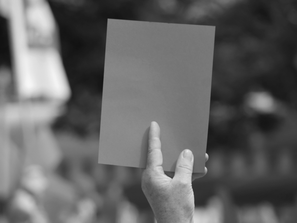 Das s/w-Foto zeigt eine Hand die eine einzelne symbolische rote Karte hochhält.